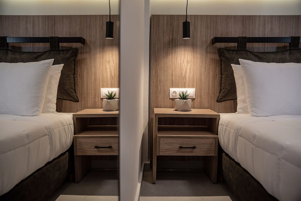 Ein Zimmer mit Spiegel, zwei Betten, Holz-Kopfteilen, Nachttischen mit Schubladen und einer kleinen Pflanze auf jedem Tisch.