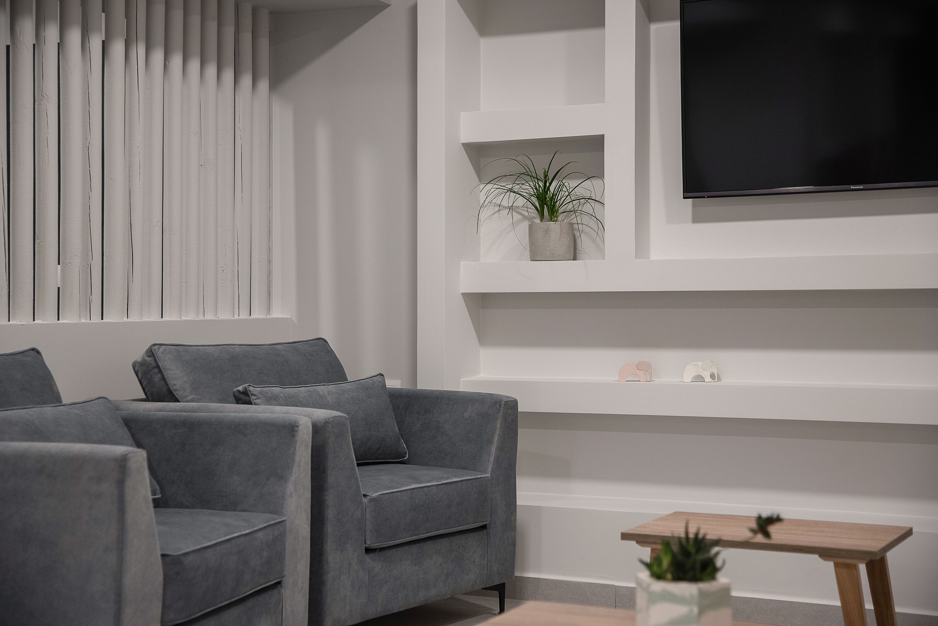 Un salon moderne avec des canapés gris, un téléviseur à écran plat, une petite table en bois et une plante en pot.