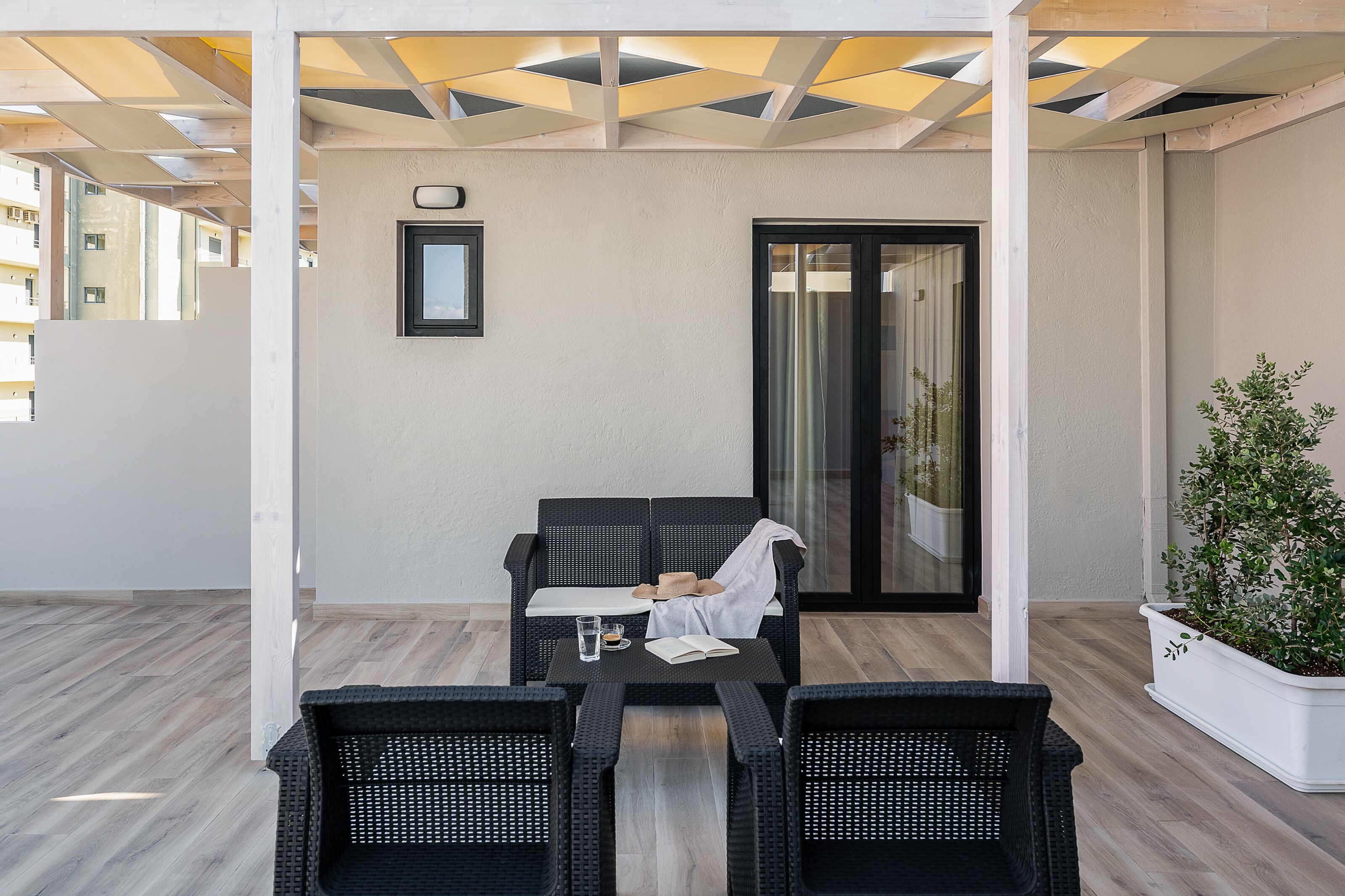 A covered outdoor seating area with a table and chairs, a sliding glass door, and a potted plant.