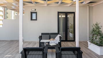 A covered outdoor seating area with a table and chairs, a sliding glass door, and a potted plant.