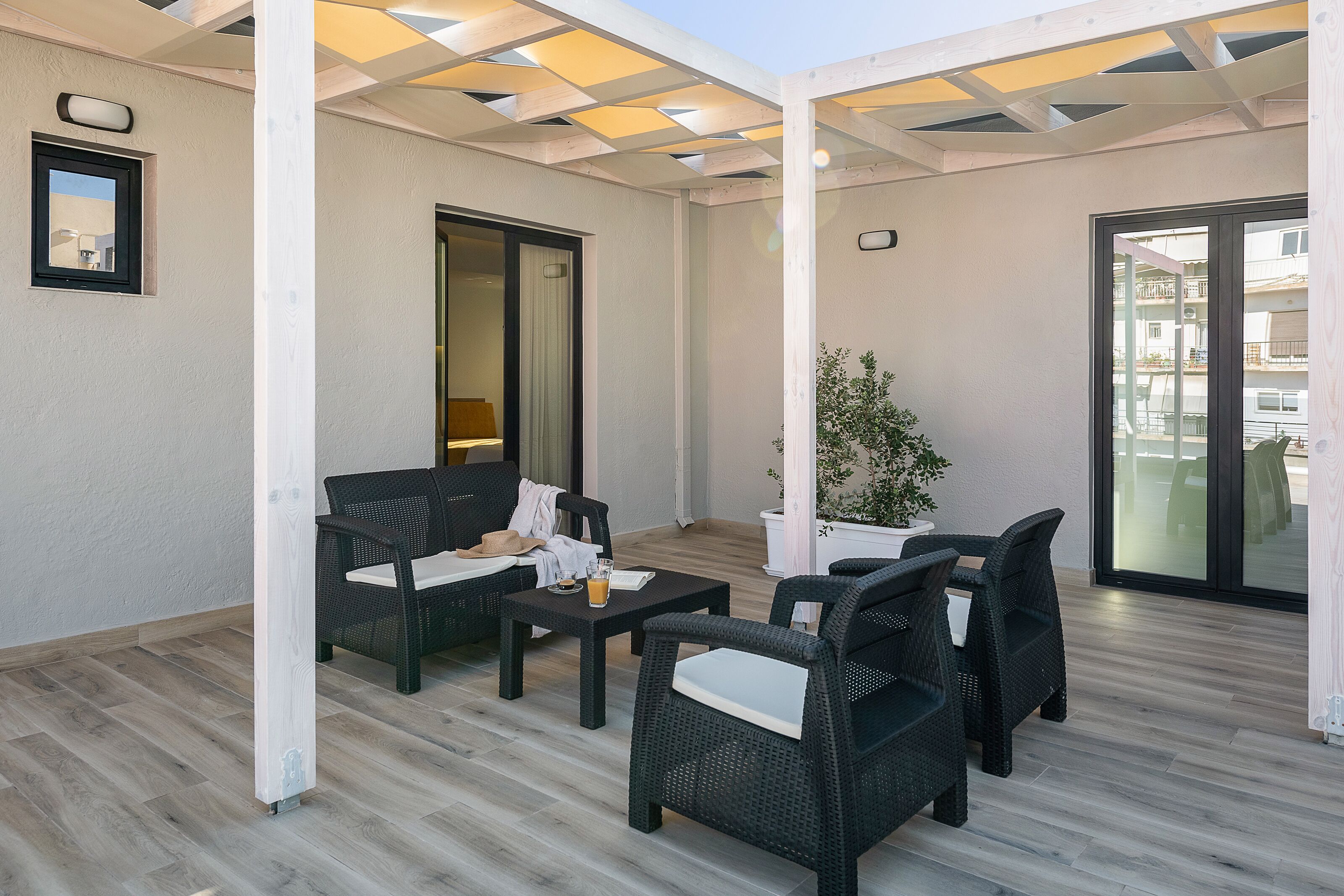 Un espacio de patio al aire libre con muebles de mimbre, una planta en maceta y un ventanal corredera que da a un balcón.
