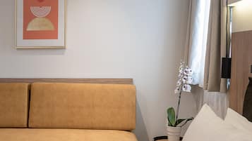 Una habitación de hotel moderna con un sofá color beige, una cama blanca, una obra de arte enmarcada en la pared, una orquídea en maceta y una mesita auxiliar pequeña.