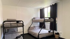 A dormitory room with bunk beds, a window with curtains, and a waste bin.