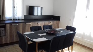 Un coin repas avec une table et des chaises, un téléviseur posé sur un meuble, et une fenêtre avec des rideaux.