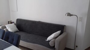 Un salon avec un canapé gris, deux coussins blancs, une table d’appoint et un lampadaire.