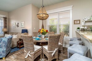 A dining area with wicker chairs, a round table, and a hanging light fixture.