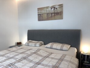 A bedroom with a bed, a nightstand, a lamp, and a painting on the wall.