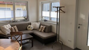 A cozy living room with a sectional sofa, a wooden table, and a coat rack. - Cozy barrier-free FEWO in new building directly between vineyards and the Main river (Segnitz)