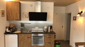 A compact kitchen with wooden cabinets, a built-in oven, a sink, and a coffee maker. - Cozy barrier-free FEWO in new building directly between vineyards and the Main river (Segnitz)