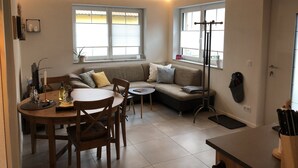 A cozy living room with a round wooden dining table, a sofa with cushions, and a floor lamp. - Cozy barrier-free FEWO in new building directly between vineyards and the Main river (Segnitz)