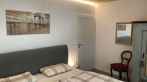 A bedroom with a bed, a nightstand, a chair, a wardrobe, a door, and a wall-mounted picture. - Cozy barrier-free FEWO in new building directly between vineyards and the Main river (Segnitz)