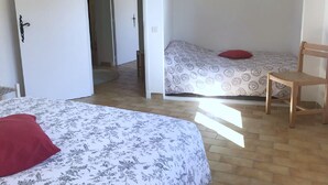 Ett rum med två sängar, den ena med ett blommigt överkast och den andra med ett geometriskt mönster. Det står en trästol och ligger en röd kudde på den ena sängen.