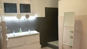 Ett badrum med ett vitt handfat, två speglar, en duschhörna och en toalett.