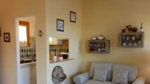 Een woonkamer met een bank, een salontafel, een zichtbare keuken door een open deur, en decoratieve objecten aan de muur.