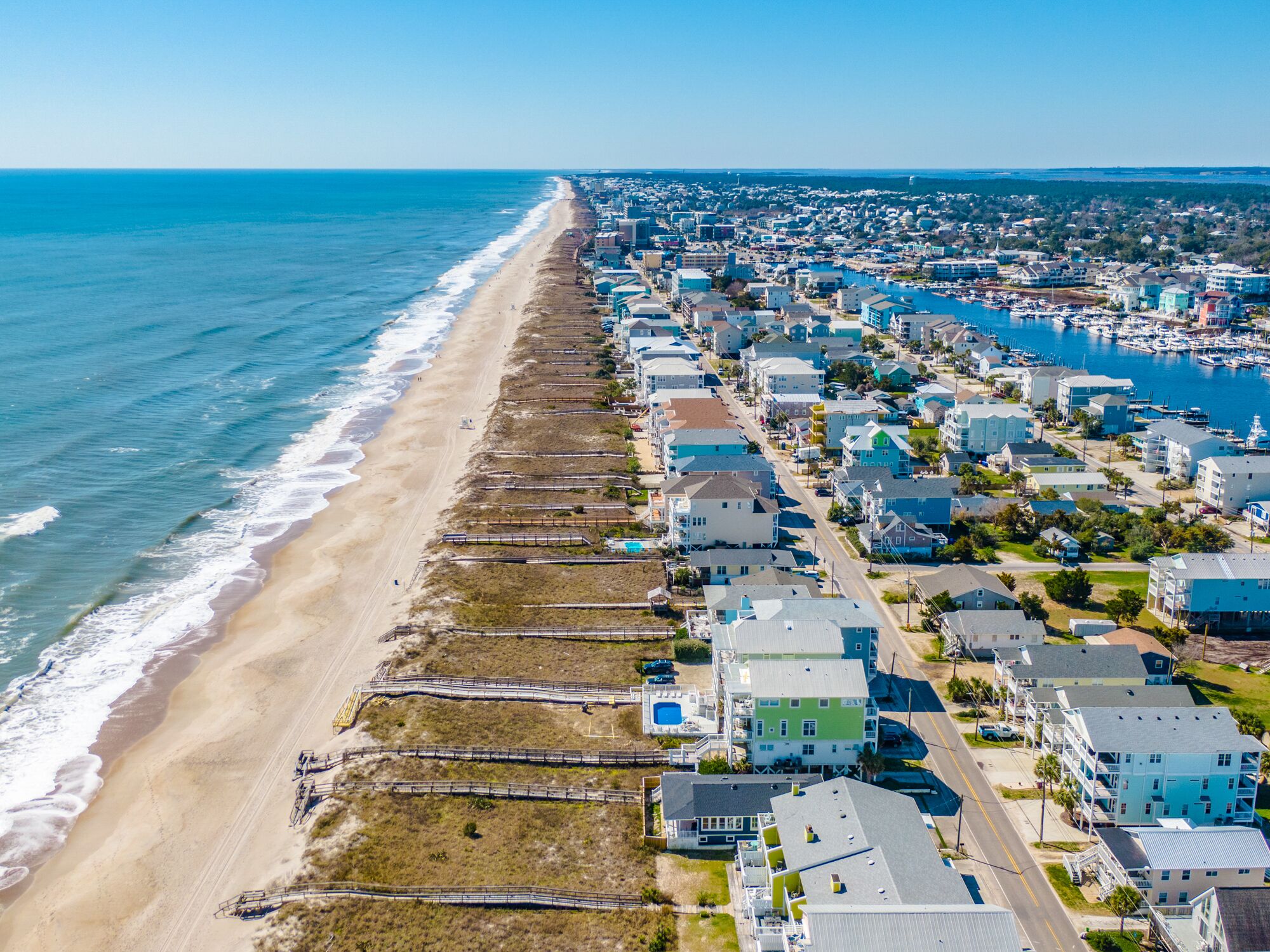 An aerial view of a coastal town with a beach, residential buildings, and a marina.