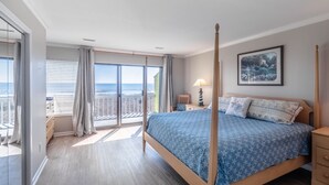 Un dormitorio con cama con dosel, un balcón con vistas a la playa y un cuadro en la pared.