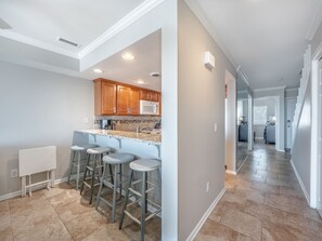 A modern kitchen with bar stools, a microwave, and wooden cabinets.