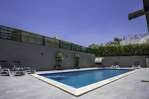 A rectangular swimming pool with a tiled edge, surrounded by lounge chairs and potted plants.