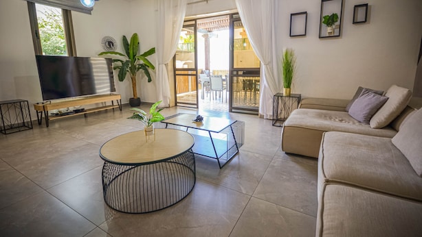 A living room with a TV, sofa, coffee table, and potted plants. - YalaRent Caesar's Villa - Families only (Eilat)