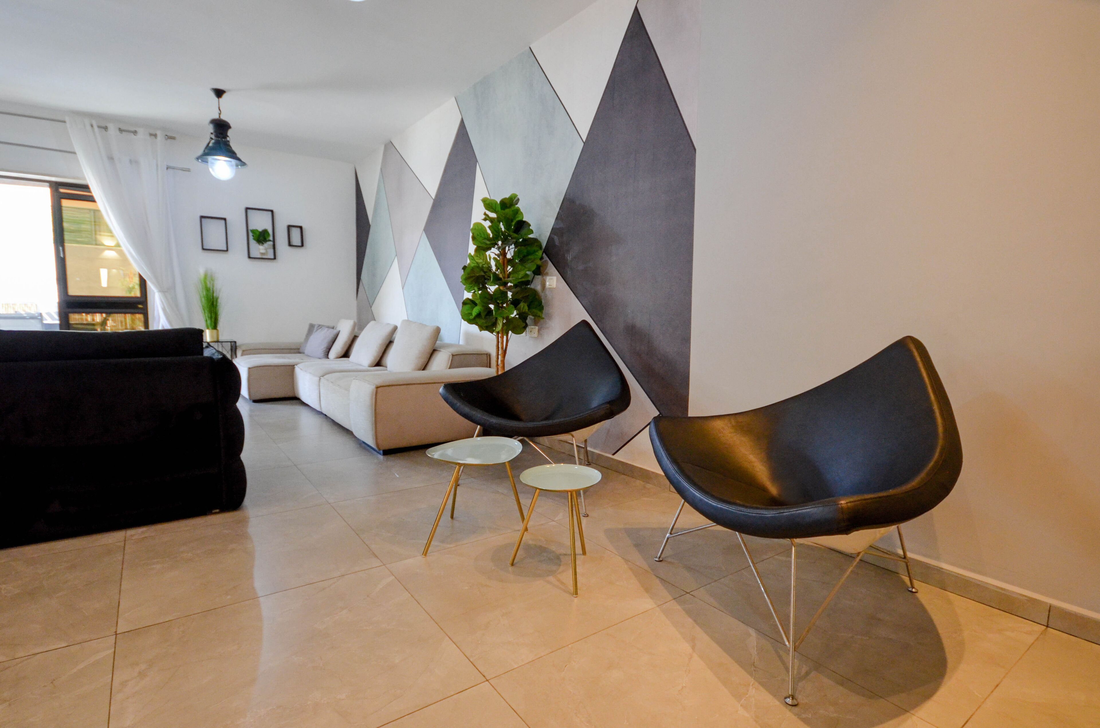A modern living room with a black sofa, two black chairs, a small white table, and a potted plant.