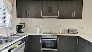 A modern kitchen with dark cabinets, a built-in oven, a coffee maker, and a dishwasher.
