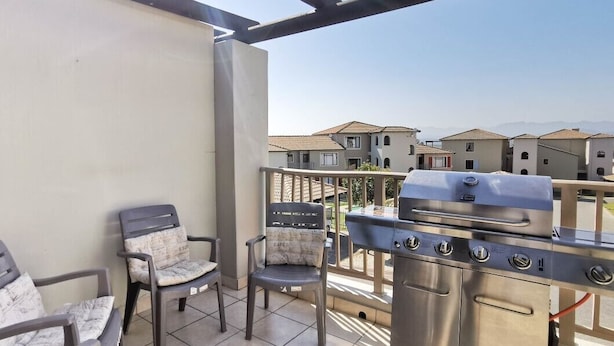 A balcony with a grill, two chairs, and a view of neighboring buildings.