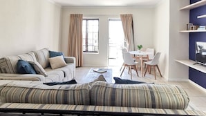 A living room with a striped sofa, a dining table with chairs, and a TV on a stand.
