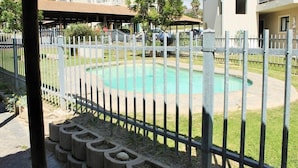 A swimming pool surrounded by a white fence, with a covered area and buildings in the background.