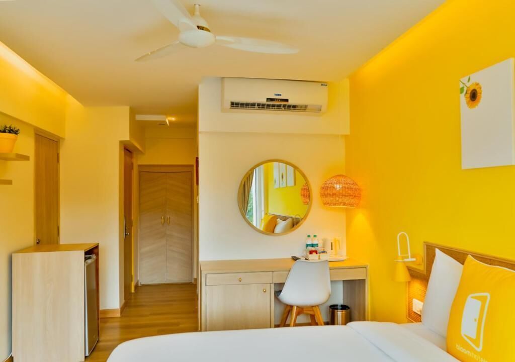 Quarto de hotel com cama, escrivaninha, cadeira e ventoinha no teto.