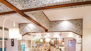 A cozy restaurant with wooden furniture, patterned ceiling, and a tiled floor. - Bloom Hotel Juhu (Mumbai)
