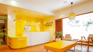 A modern reception area with a bright yellow color scheme, a reception desk, seating area, and a large window providing a view of the outdoors. - Bloom Hotel Juhu (Mumbai)