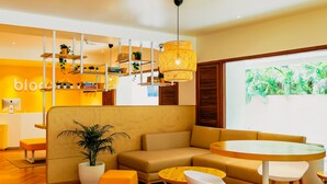 A modern living room with a sofa, ottomans, a round table, and a potted plant. - Bloom Hotel Juhu (Mumbai)