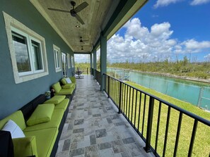 A covered balcony with green cushioned seating, a ceiling fan, and a view of a water body. - Beautiful Villa in Lucaya, Freeport Bahamas (Freeport)