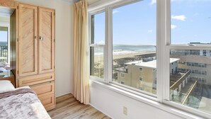 Quarto com uma grande janela com vista para uma praia e edifícios.