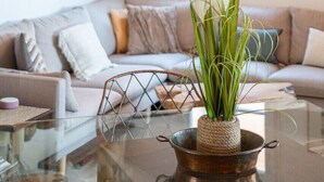 Ein modernes Wohnzimmer mit einem Glastisch, einer gewebten Pendelleuchte und einem Blumentopf.