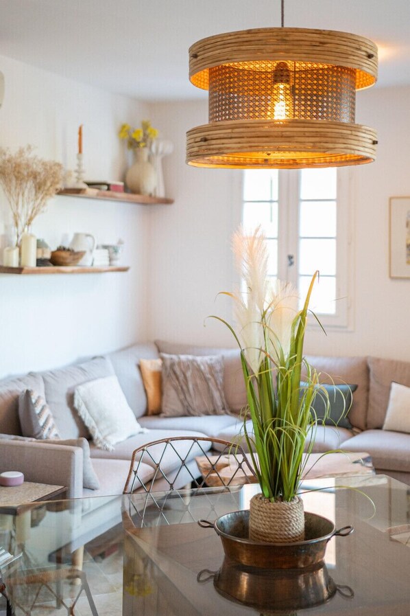 A modern living room with a glass coffee table, a woven pendant light, and a potted plant.