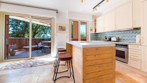 Eine moderne Küche mit einer großen Kochinsel, Schiebetüren zu einer Terrasse und Blick ins Freie.