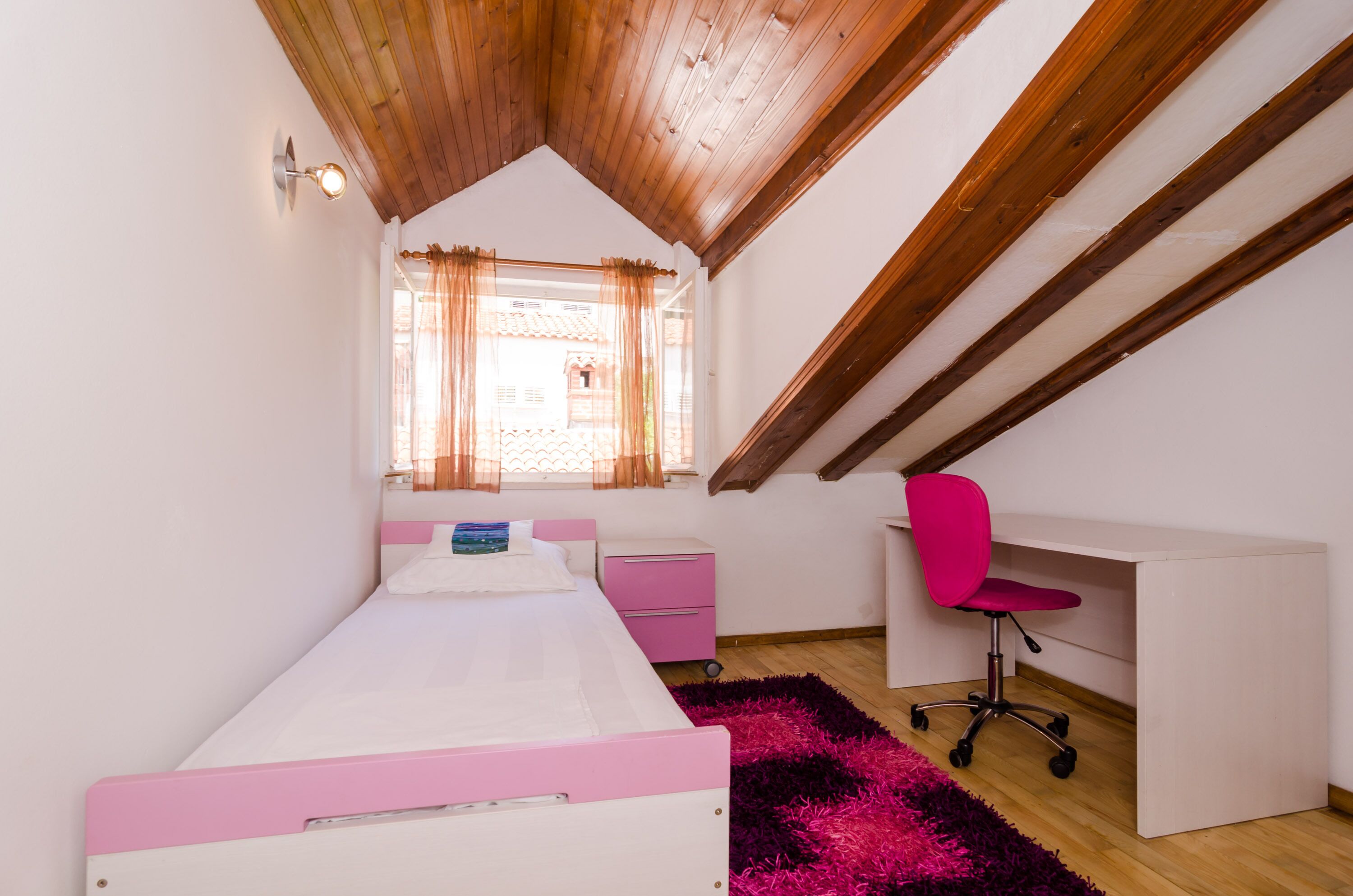 A bedroom with a bunk bed, a desk, a chair, and a window with curtains.