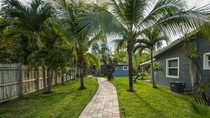 A paved pathway in a backyard with palm trees and a house. - Charming Oasis with a Pool (Fort Lauderdale)