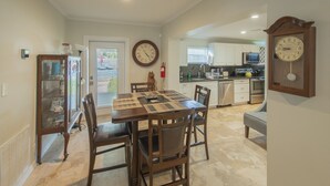 A dining area with a wooden table and chairs, a clock on the wall, and a kitchen in the background. - Charming Oasis with a Pool (Fort Lauderdale)
