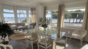 En matplats med ett glasbord, vita stolar och utsikt över havet genom stora fönster.