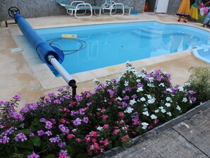 Uma piscina com uma mangueira azul, rodeada por um canteiro de flores com flores cor-de-rosa e brancas.