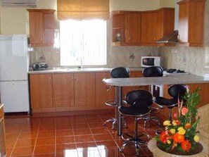 Uma cozinha com armários de madeira, uma geladeira branca, um micro-ondas e um espaço de refeições com uma mesa e cadeiras.