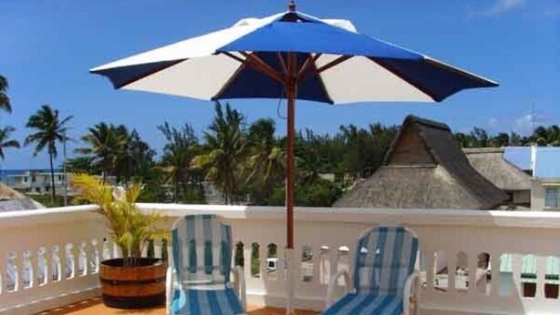 A balcony with two striped lounge chairs and a blue umbrella.