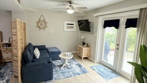 Un salon avec un canapé bleu, une petite table ronde, un ventilateur de plafond et un téléviseur fixé au mur.