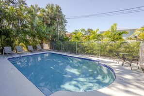 Une piscine dont le bord est recouvert de carreaux, entourée d’une clôture en treillis métallique et ombragée par des palmiers.
