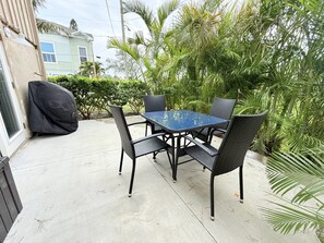 Une terrasse extérieure avec une table et des chaises, entourée d’une végétation luxuriante et avec une maison en arrière-plan.