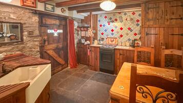 A rustic kitchen with wooden cabinets, a stone wall, and a tiled backsplash.