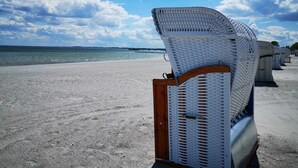 Ein Strand mit weißen Korbstühlen, die entlang der Küste zum Meer hin ausgerichtet sind.