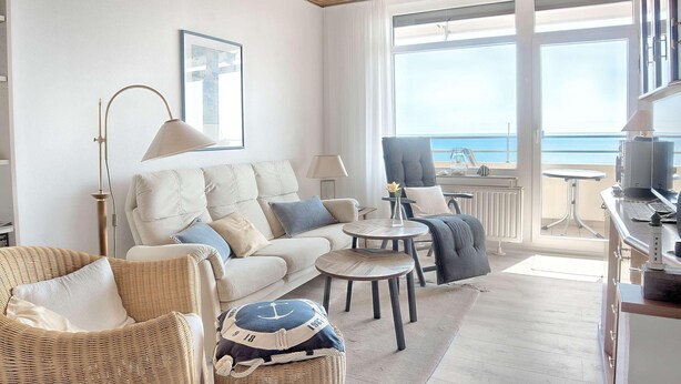 Ein modernes Wohnzimmer mit Sofa, Sesseln, einem Couchtisch und Meerblick durch große Fenster.